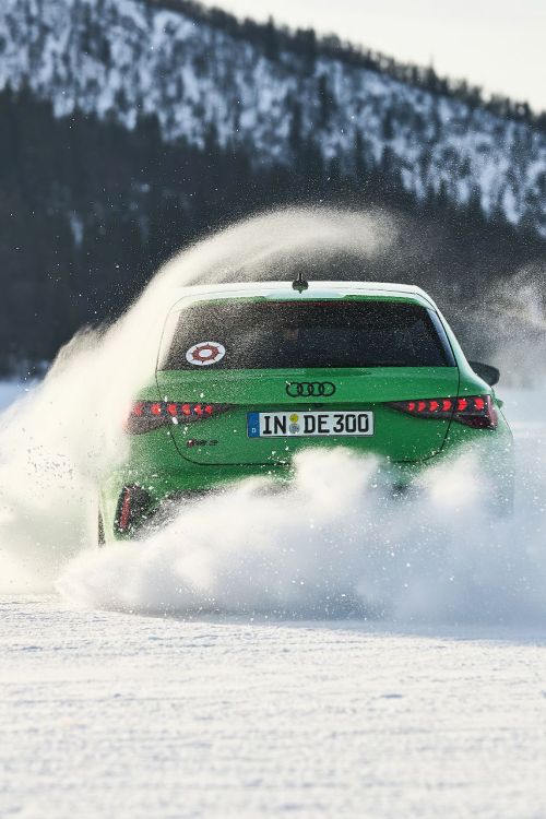 Ein grüner Audi driftet dynamisch über eine verschneite Fläche während der Audi Driving Experience, umgeben von schneebedeckten Bergen und Wäldern.